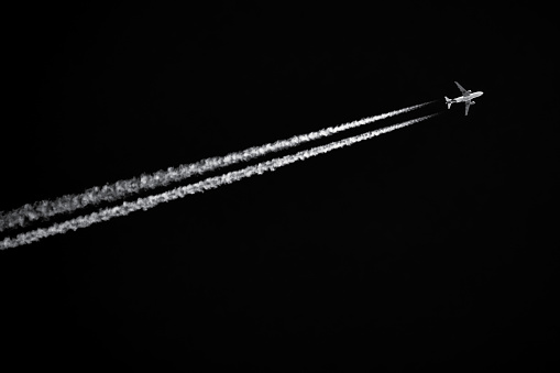 Twin-engined jetliner with contrails flying in black sky. Air travel background with copy space.