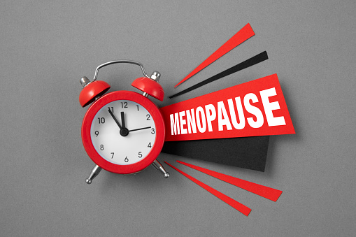 Red alarm clock with papers and text menopause on gray background