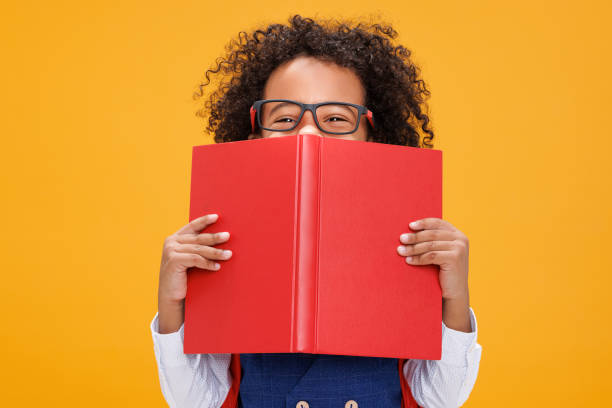 istock Happy sly curly schoolboy  looks out from behind the book 1420804078