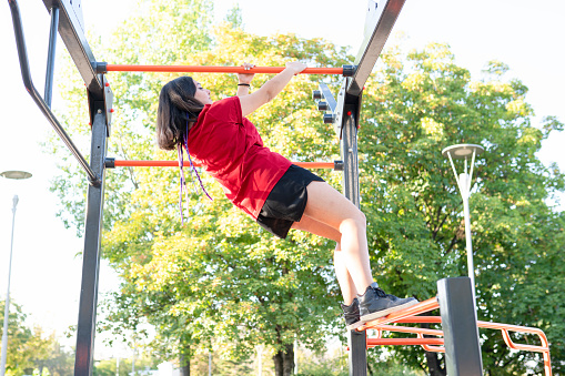 young woman playing on outdoor playground. Active young woman on colorful monkey bars. Healthy summer activity for people. people climbing.