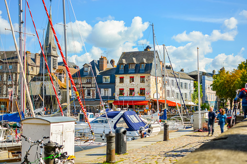 Boats, yachts and fishing vessels line the old harbor or Vieux Bassin in the charming Normandy village of Honfleur, France, with cafes and shops surrounding the marina.