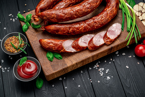 Dry appetizing smoked pork sausage on a dark background with different spices and vegetables. Photo for the menu
