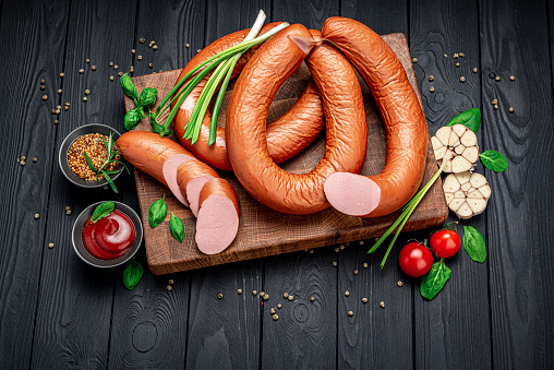 Dry appetizing smoked pork sausage on a dark background with different spices and vegetables. Photo for the menu