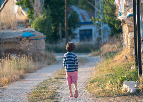Rear photo of 9 years old elementary school boy walking on the road in village. Village houses are seen around. Shot under daylight with a full frame mirrorless camera.