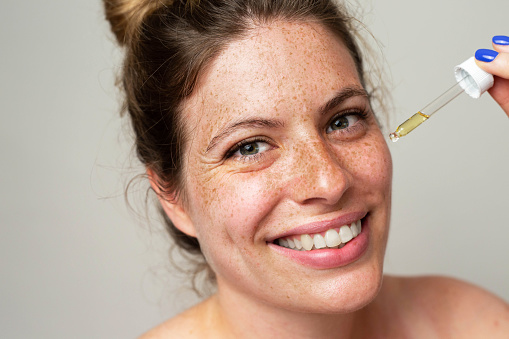 A beautiful woman with freckles applies serum to her face with a pipette