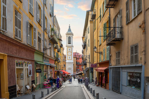 one of the picturesque narrow alleys and streets of shops and cafes in the old town vieux nice district of the city of nice, france, on the cote d'azur french riviera along the mediterranean sea. the bell tower of the nice cathedral in view. - city of nice restaurant france french riviera imagens e fotografias de stock