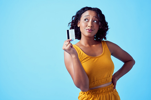 Thinking black woman shopping with credit card, doing retail therapy and banking with debit card standing against blue studio background. Person with financial idea and advertising finance management