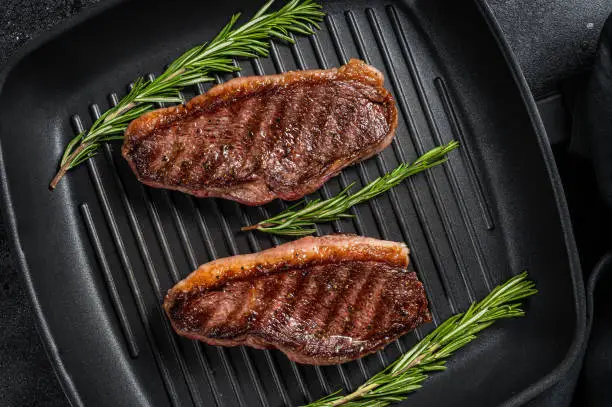 Grilled Top sirloin beef steak or brazilian Picanha, roasted meat on grill pan. Black background. Top view.