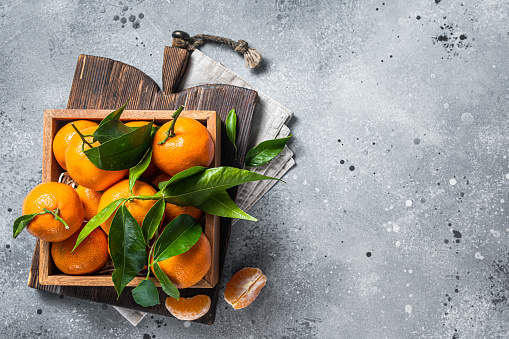 Organic Tangerines, mandarins with green leaves in wooden box. Gray background. Top view. Copy space.