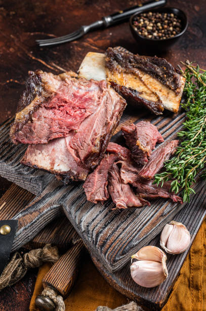 istock Braised veal beef short ribs on wooden cutting board with thyme. Dark background. Top view 1420823962