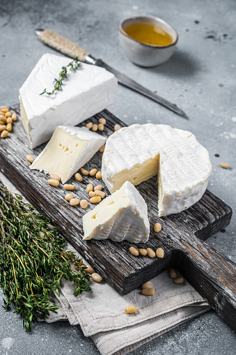 Delicioso brie de queso y camembert sobre tabla de madera con hierbas y frutos secos. Productos lácteos franceses. Fondo gris. Vista superior photo