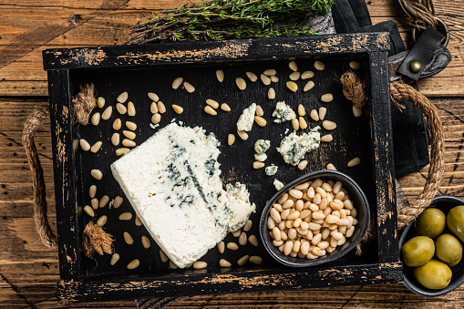 Gorgonzola cheese in a wooden tray with olives and nuts. Wooden background. Top view.