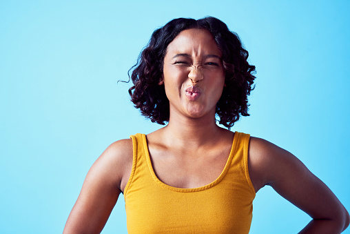 Funny emoji girl with comic nose and lips expression on her face on a studio blue background. Comedy young and unique woman with stink, ew or crazy face for a humor, colorful and human portrait