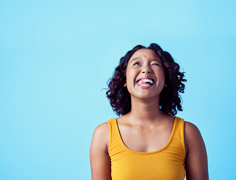Happy black woman with a smile and funny face with tongue out over teeth, with a blue background. Fun crazy girl, excited about beauty and female independence. Celebration of love, life and freedom.