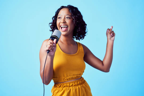 istock Happy woman singing with microphone and smile against blue studio mockup background. Young professional singer sing to music with performance with a mic while having fun and dance to the rhythm 1420842142