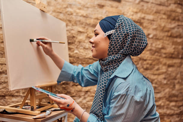istock A woman in a hijab paints on canvas with a brush and tempera 1420844973