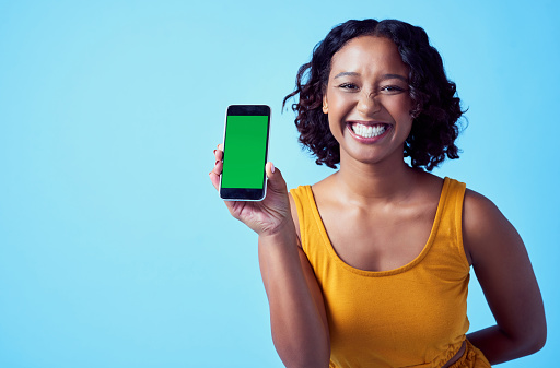 Green screen on phone app for marketing, advertising and mobile brand mockup space on blue color studio background. Portrait of a happy woman with internet technology for social media website contact