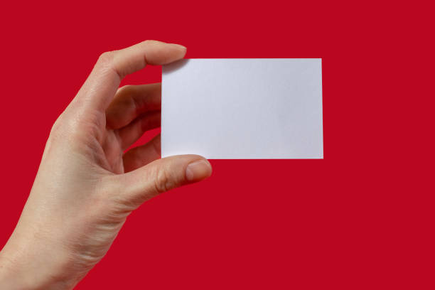 istock Human hand holds a blank sheet of paper on a red background with blank space for text 1420845314
