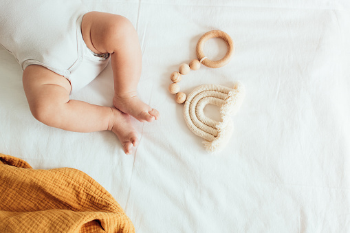 Baby playing with a wooden toy on white linens background. Top view. Copy space.