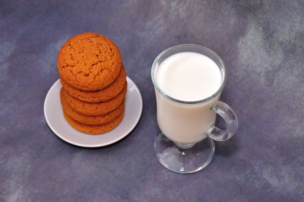 una pila di biscotti di farina d'avena fresca su un piattino e un bicchiere di latte caldo su uno sfondo astratto grigio. - oat oatmeal isolated stack foto e immagini stock