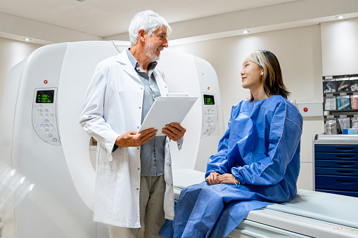 Medium-shot of male doctor explaining MRI scan procedure to female Asian-American patient inside a diagnostic facility