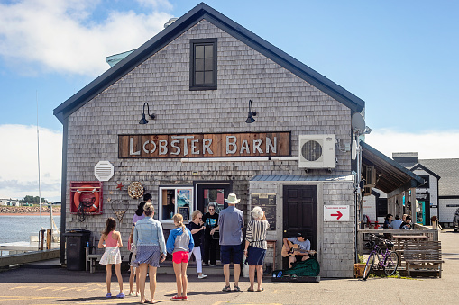 Victoria by the Sea, Canada - August 24, 2022. A line-up forms alongside a busker outside of the Lobster Barn, one of the top-rated eateries in Victoria by the Sea, Prince Edward Island.