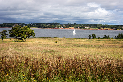 A sailboat passes between Stratford and  Skmaqn–Port-la-Joye–Fort Amherst National Historic Site, Prince Edward Island
