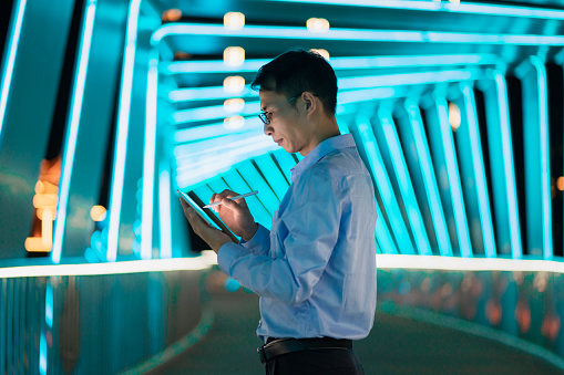 A man holds a digital pen and uses a tablet against the background of cyan neon lights