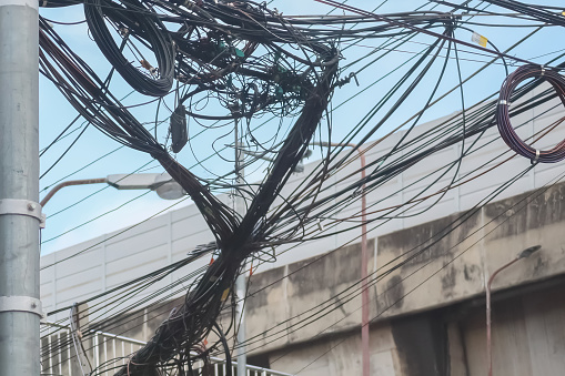 Image of communication cable wires and internet fiber signal line crossing chaos on blurry background of elevated expressway in Bangkok, Thailand.