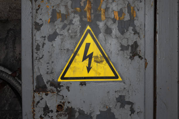 High Voltage Sign. Black Arrow in Yellow Triangle on Rusty Gray Painted Metal Surface.