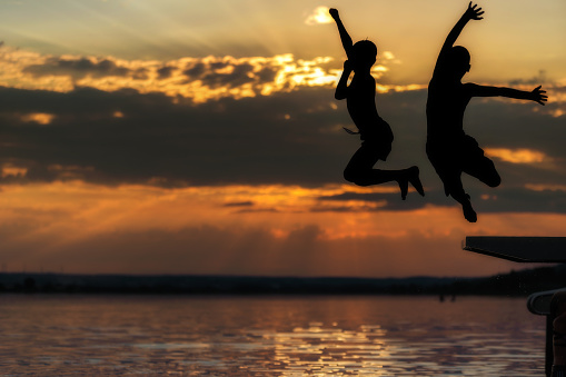 silhouettes of two unrecognizable boys - jumping into the water at sunset - part of a series