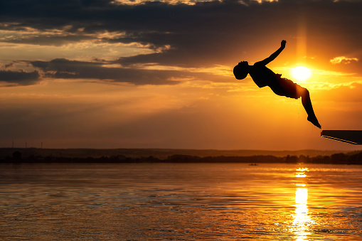 silhouettes of one unrecognizable boy - jumping into the water at sunset - part of a series