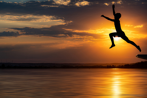 silhouettes of one unrecognizable boy - jumping into the water at sunset - part of a series