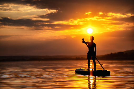 Silhouette of an unrecognizable boy standing on a stand up paddle board at sunset - part of a series