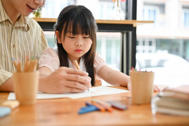 istock Pretty young Asian girl concentrating doing homework, having an art class with her private teacher. 1420908582