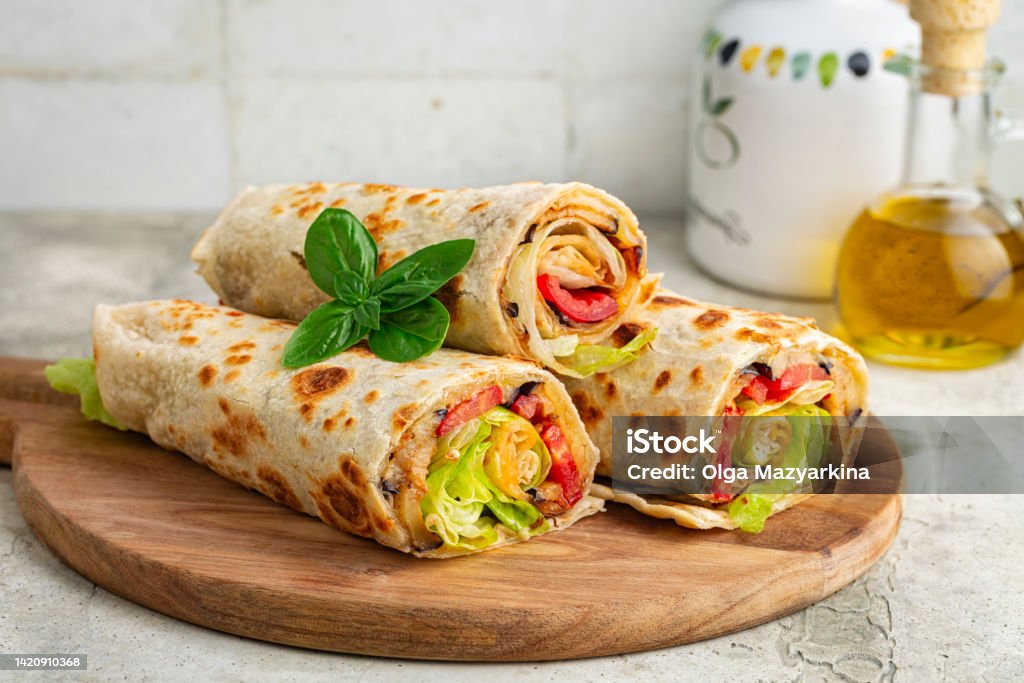 Wraps with a soft flatbread rolled around a filling with vegetables and cheese, tomato, fried eggplant, lettuce. Vegetarian food concept. Light background. Piadina Stock Photo