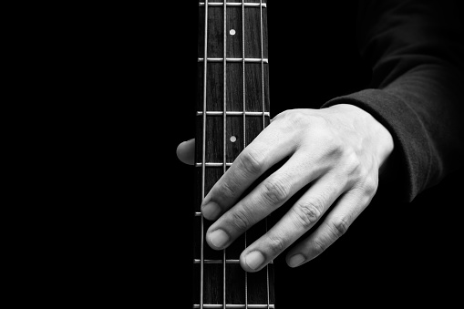 black and white close up male musician hand on bass guitar fingerboard, isolated on black. music background