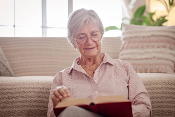 istock Attractive senior woman sitting on the floor at home while reading a book 1420912909