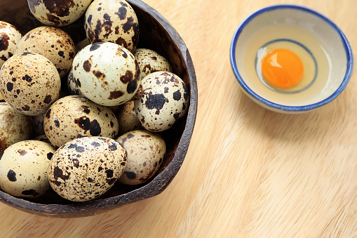 Yolk quail egg without shell and raw quail eggs in wooden bowl on wood table. top view