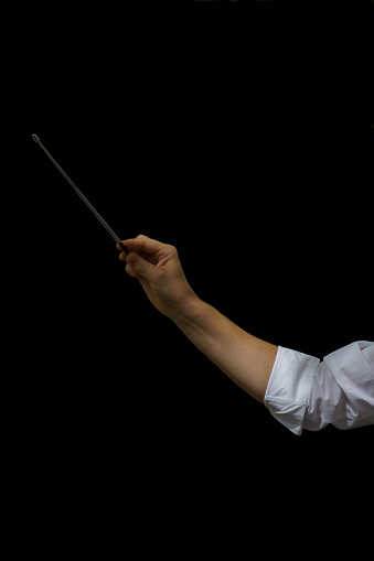 arm of an orchestra conductor holding a baton with a white shirt on a black background