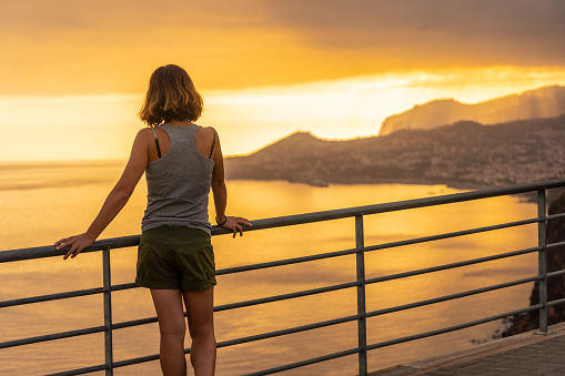 Young woman tourist at Mirador de Cristo Rei looking at the city of Funchal at sunset, Madeira