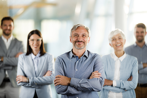 Happy, professional and corporate business people standing with arms crossed in an office together at work. Portrait of a manager leading a team and smiling with arms folded while standing in line