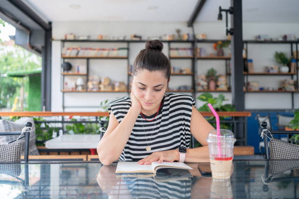 Portrait of Beautiful Woman Doing Digital Detox and Reading Book Sitting at Cafe Table