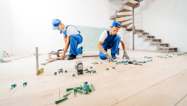 Two workers in a special uniform laying tiles with tile leveling system and laser level on the floor in a new house