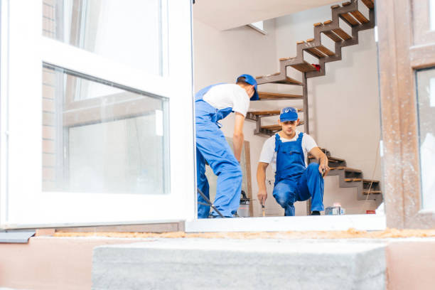 Two workers in a special uniform laying tiles with tile leveling system and laser level on the floor in a new house