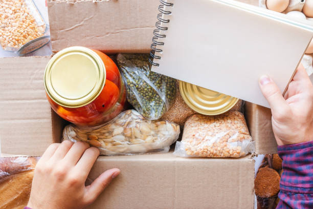 istock looks into a notebook near a donation box with different products. donation list concept 1420929799