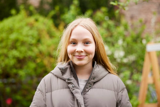 Portrait of a beautiful girl wearing warm jacket standing in backyard garden Portrait of a beautiful girl wearing warm jacket smiling at the camera standing in backyard garden. Girl enjoying a peaceful day outdoors. teenage girls pretty smile looking at camera waist up stock pictures, royalty-free photos & images