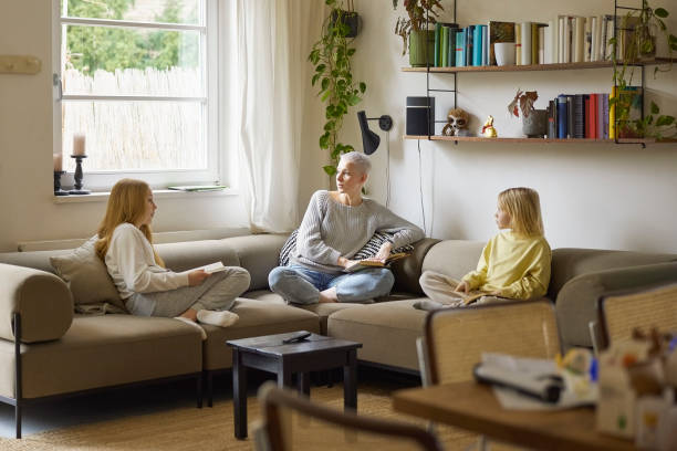 istock Mother and daughters sitting on sofa with books and talking 1420930328