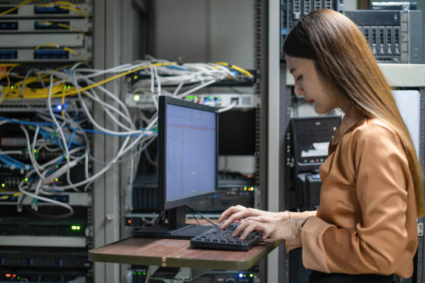 une programmeuse travaille dans une salle de serveur. la fille est debout à côté des supports informatiques du centre de données. l'administrateur regarde le moniteur avec les paramètres du réseau. - data center computer programmer women photos et images de collection