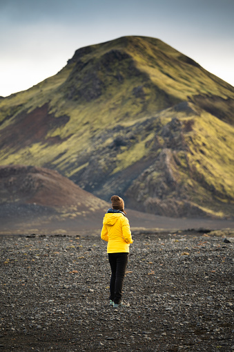 Back view of asian woman in yellow jacket standing with volcano mountain on Icelandic highlands in summer at Iceland